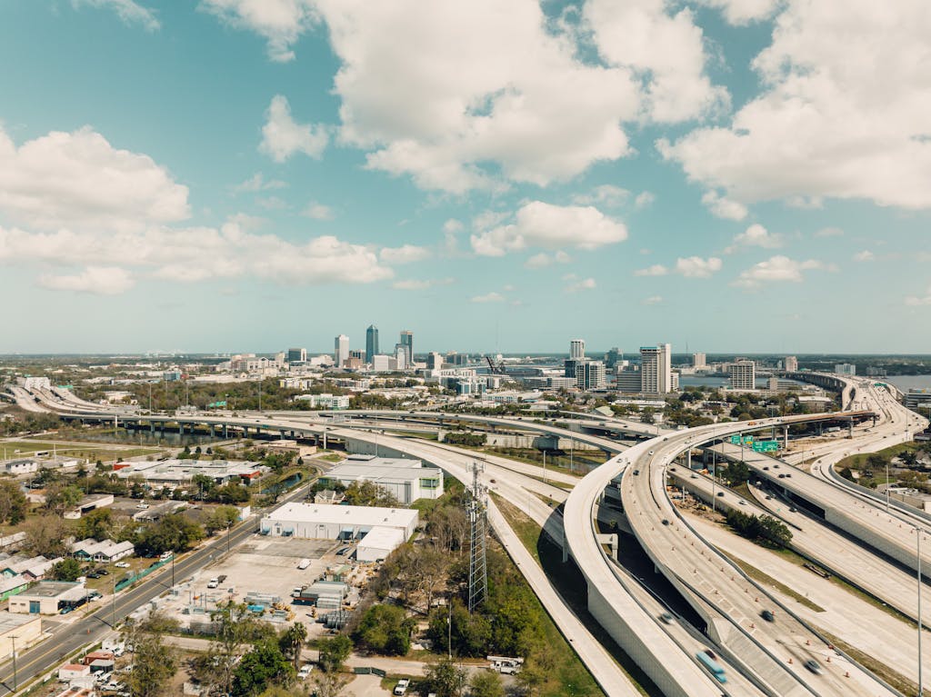 Drone shot of Jacksonville, FL skyline with complex highway network and bright sky.